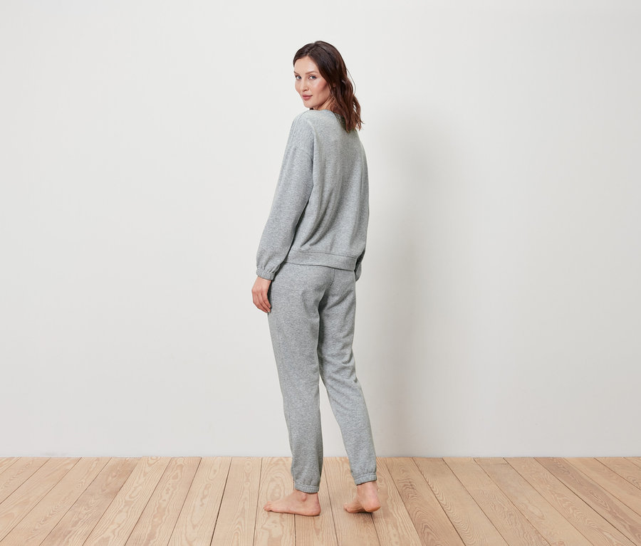 Une femme regarde par-dessus son épaule, vêtue d'un ensemble gris composé d'un sweat-shirt et d'un pantalon de jogging.