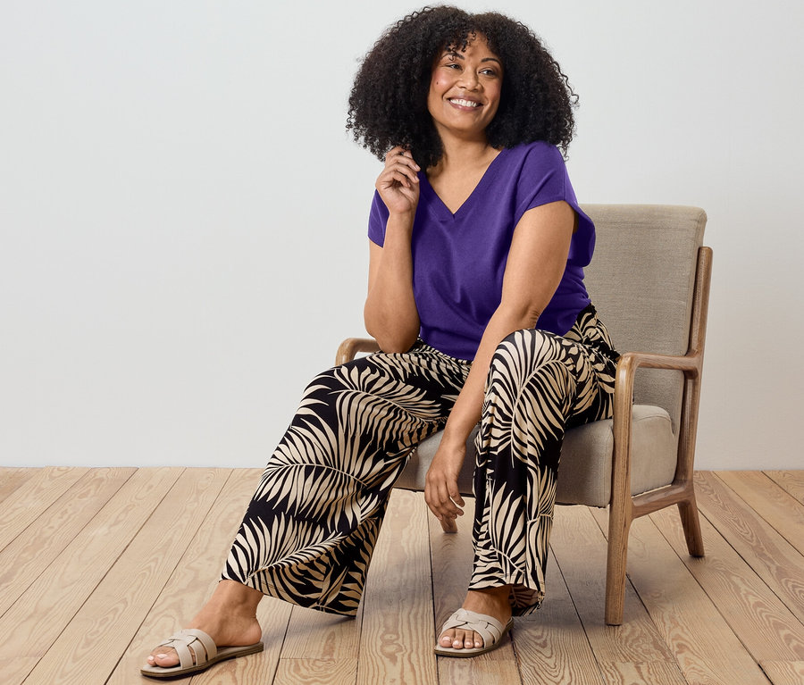 Femme assise sur une chaise portant un pull-over violet et un pantalon palazzo imprimé.