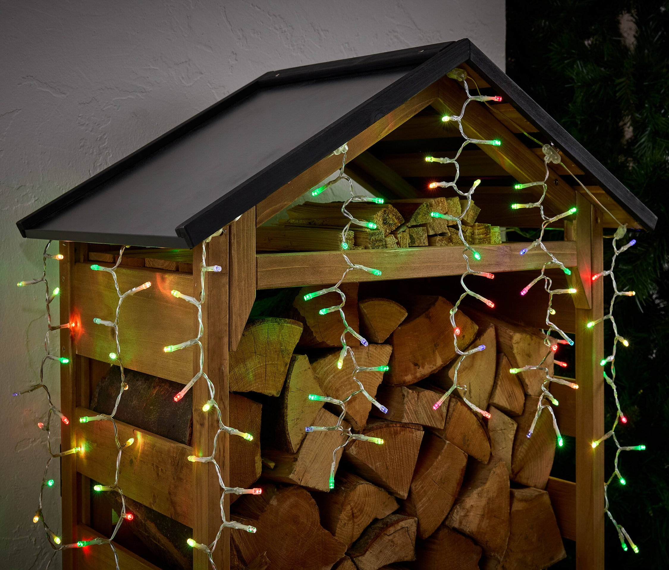 Un abri à bois rempli de bûches, décoré de lumières colorées.