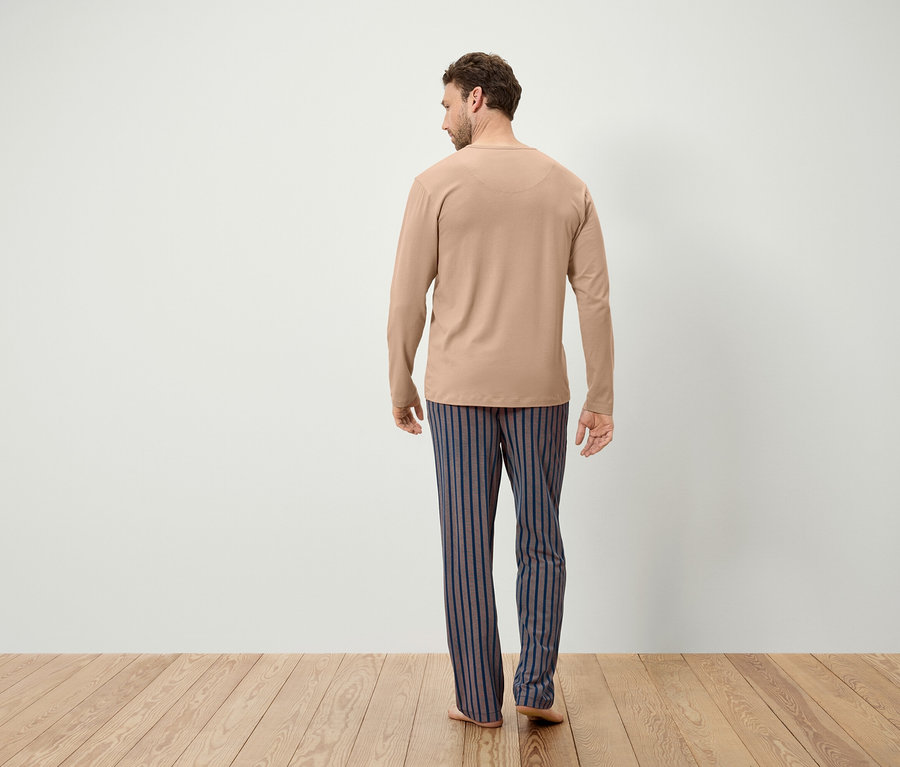 Un homme portant un t-shirt à manches longues beige et un pantalon rayé bleu-gris se tient dos à la caméra.