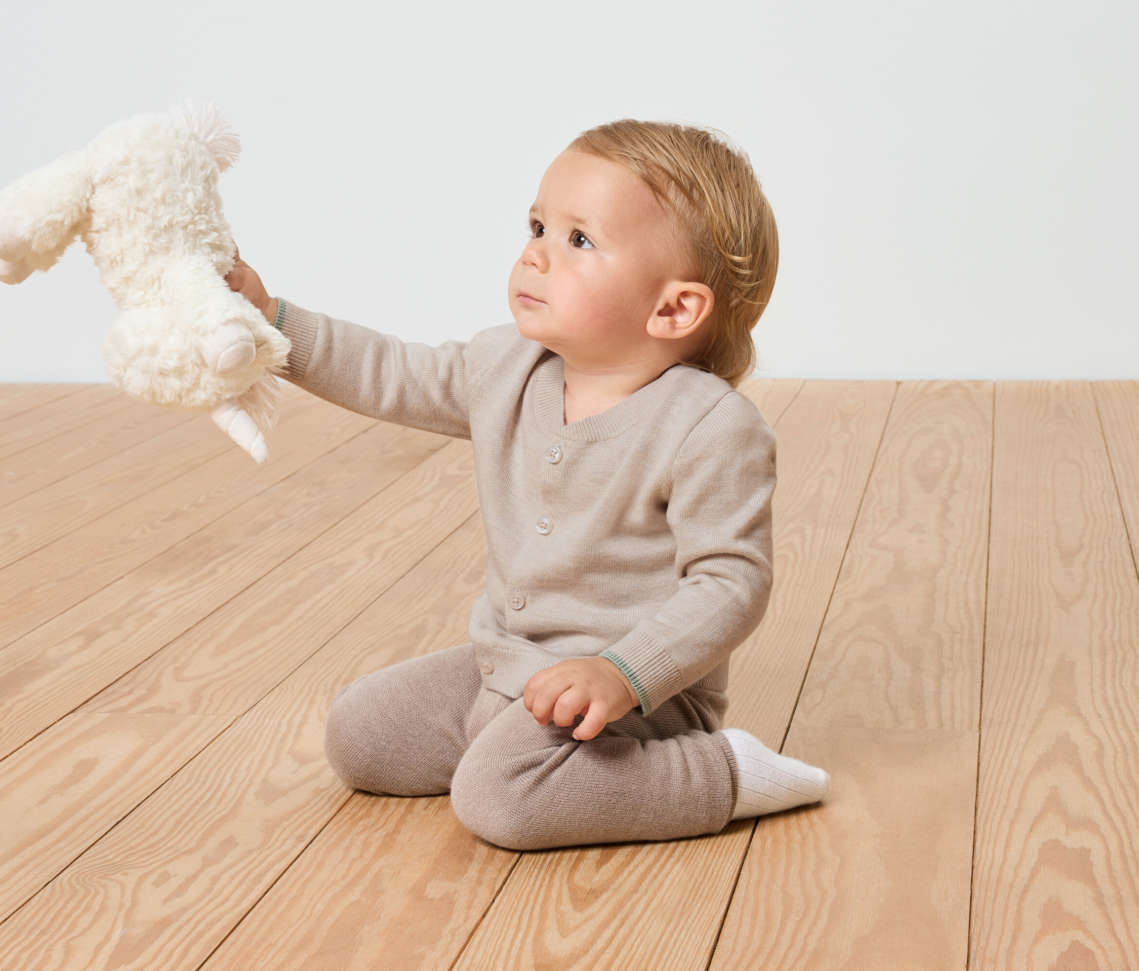 Un enfant est assis sur un plancher en bois et tient une peluche.