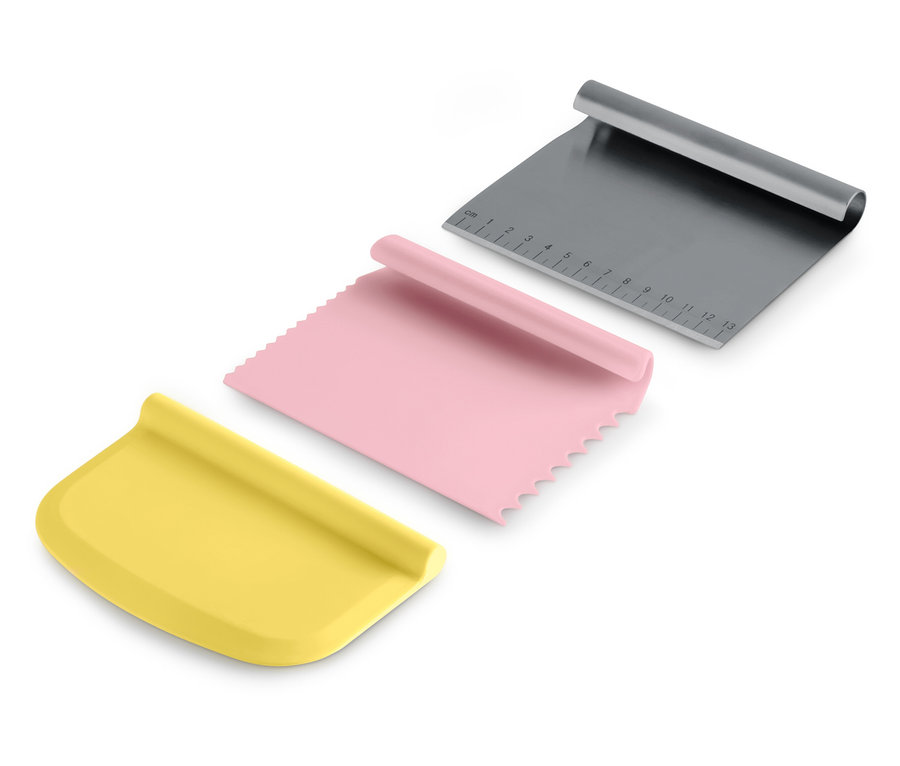 Trois grattoirs à pâte : jaune, rose et gris.