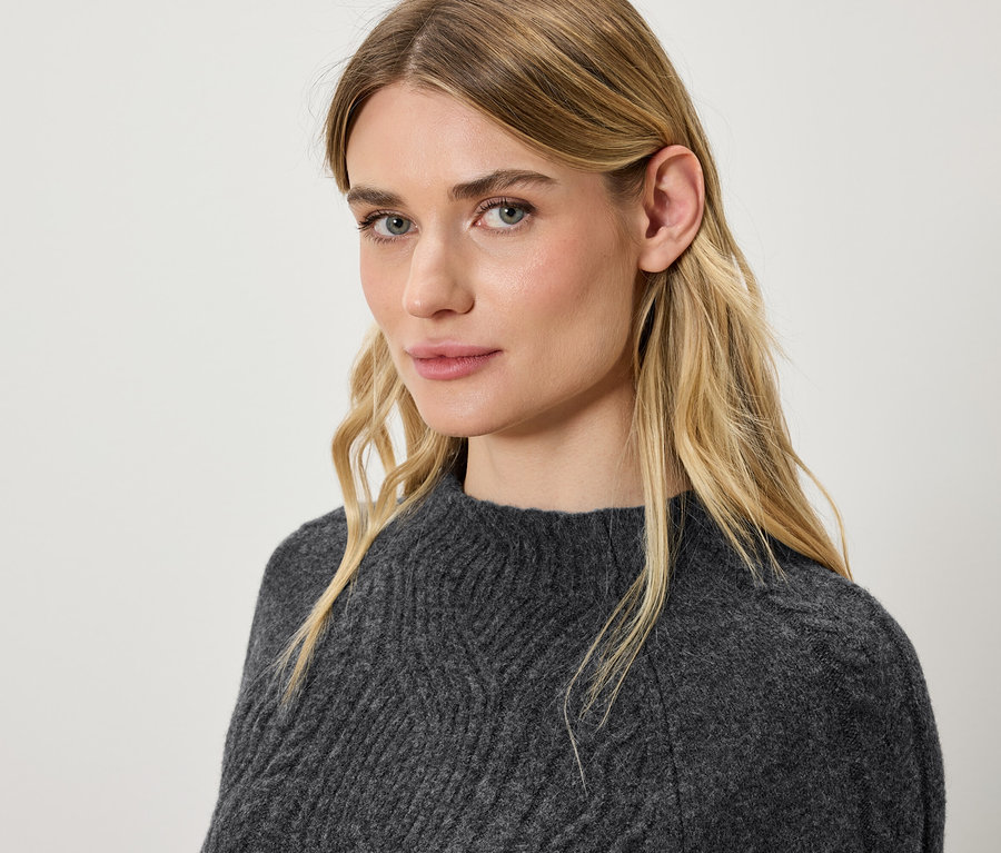 Portrait d'une femme blonde portant un pull en tricot gris.