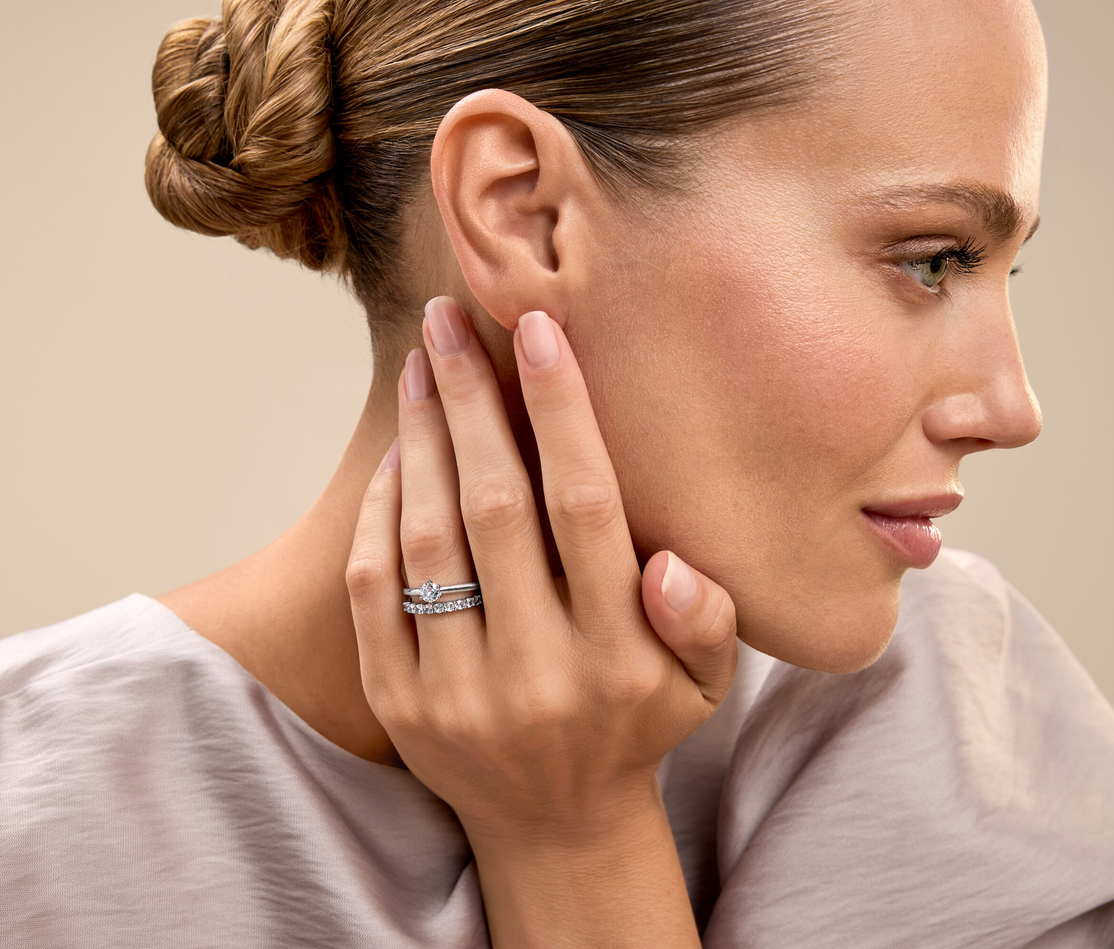 Une femme aux cheveux attachés touche son visage et montre une bague.
