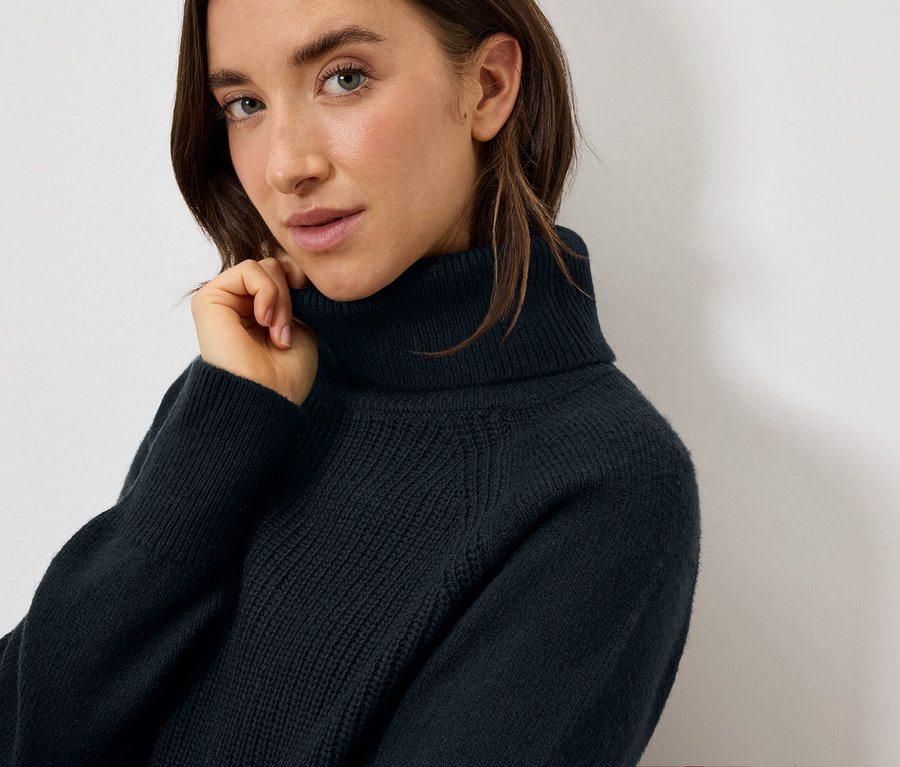Portrait d'une femme aux cheveux bruns portant un pull à col roulé bleu marine.
