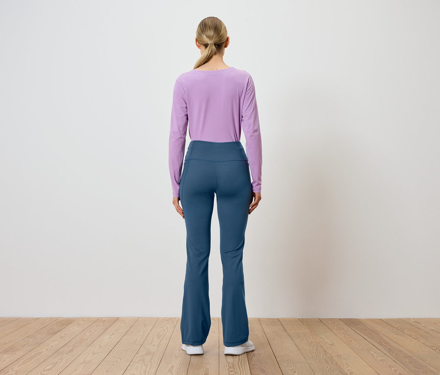 Une femme se tient dos à la caméra, portant un haut à manches longues violet et un pantalon bleu.