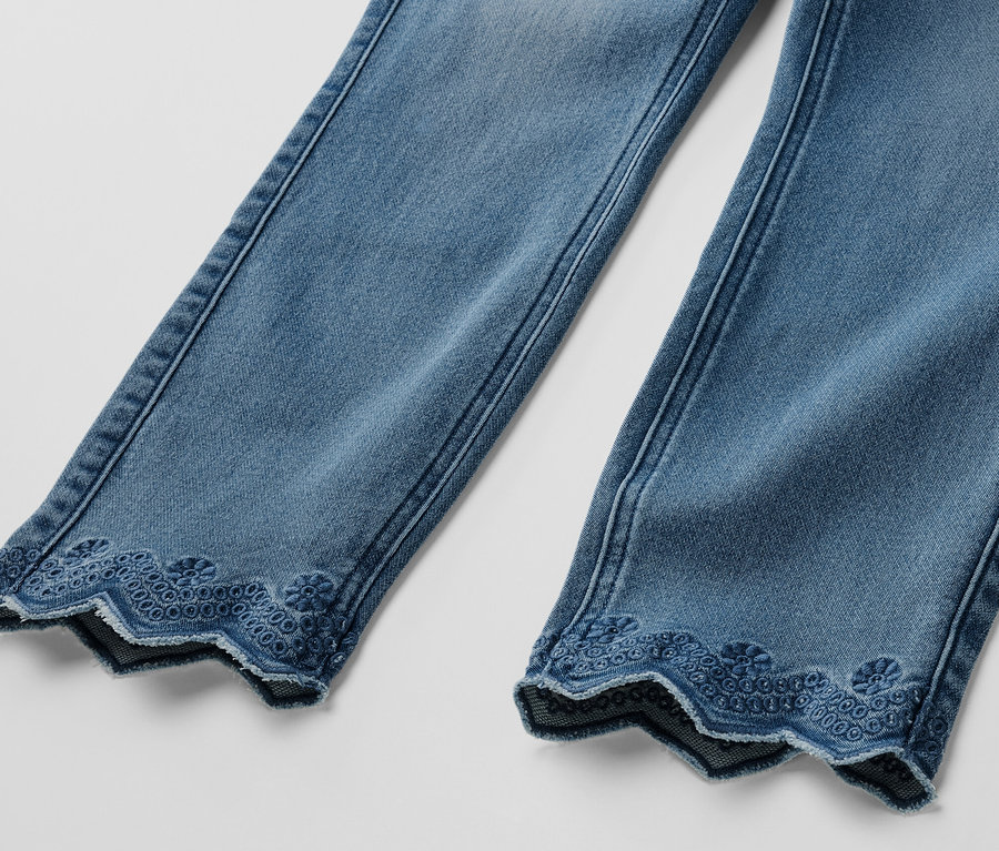 Détail de deux jambes d'un tregging 7/8 bleu clair avec broderie ajourée sur l'ourlet.
