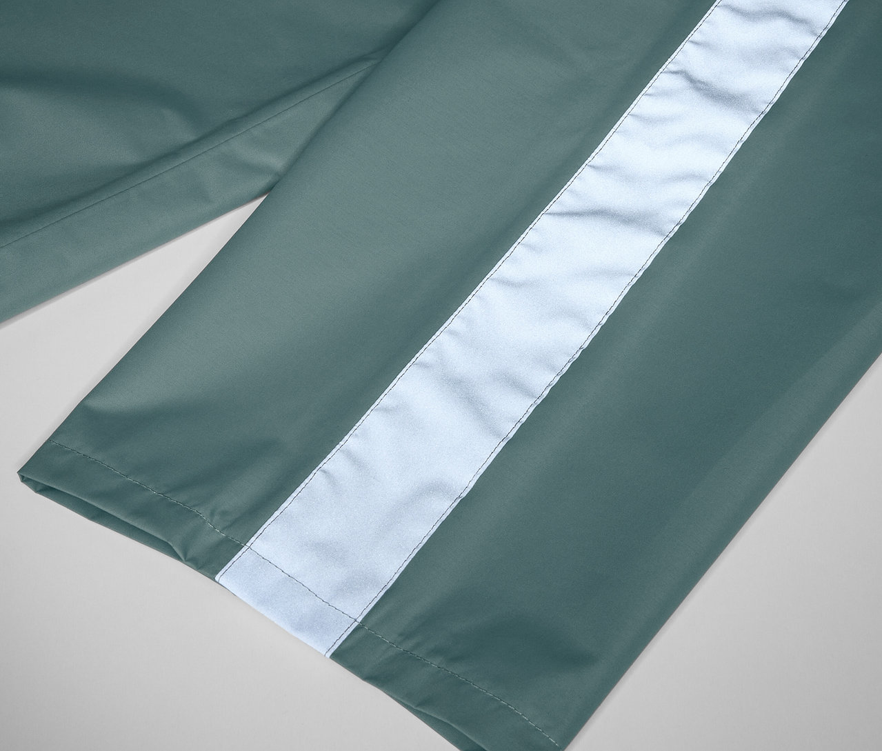 Gros plan sur un pantalon de pluie pour enfant sauge avec une bande réfléchissante.