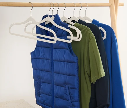 Un gilet bleu et des t-shirts suspendus à des cintres sur un portant en bois.