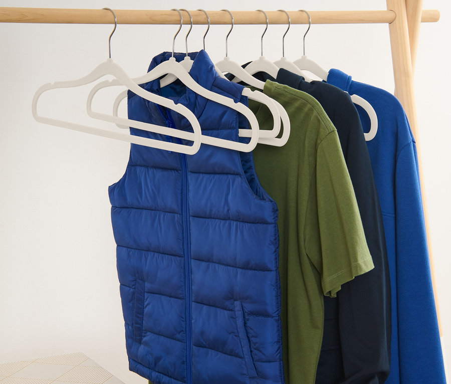 Un gilet bleu et des t-shirts suspendus à des cintres sur un portant en bois.