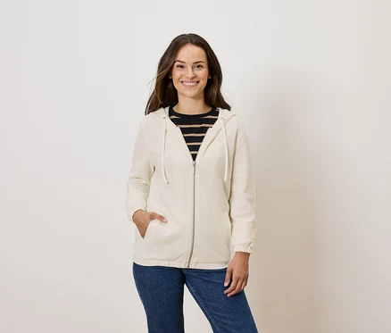 Femme posant en sweat à capuche zippé crème et jean bleu.