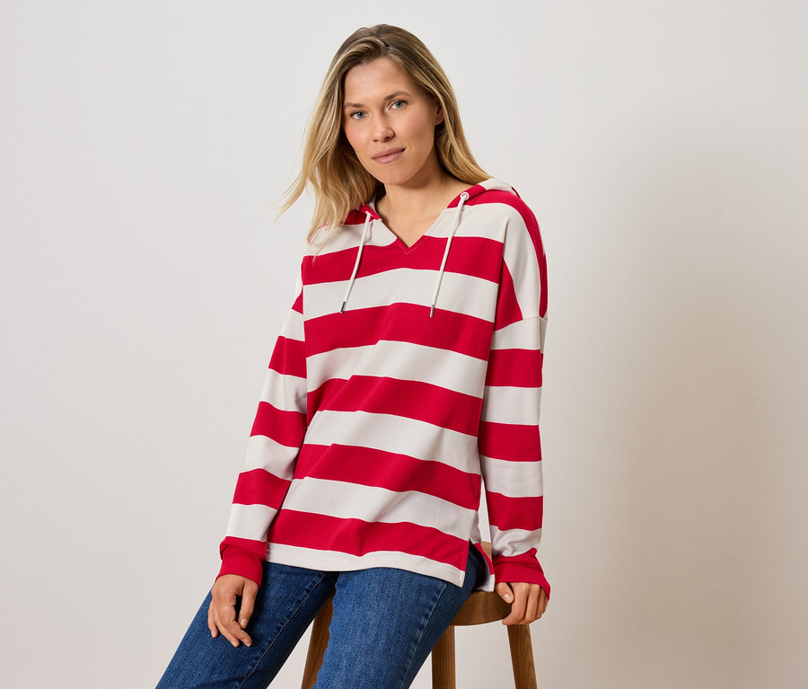 Une femme est assise sur un tabouret et porte un sweat à capuche rayé et un jean.