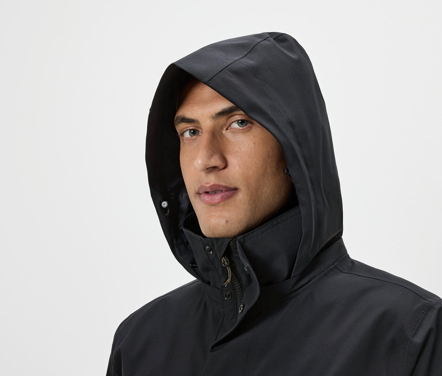 Portrait d'un homme portant un blouson noir à capuche sur un fond clair.