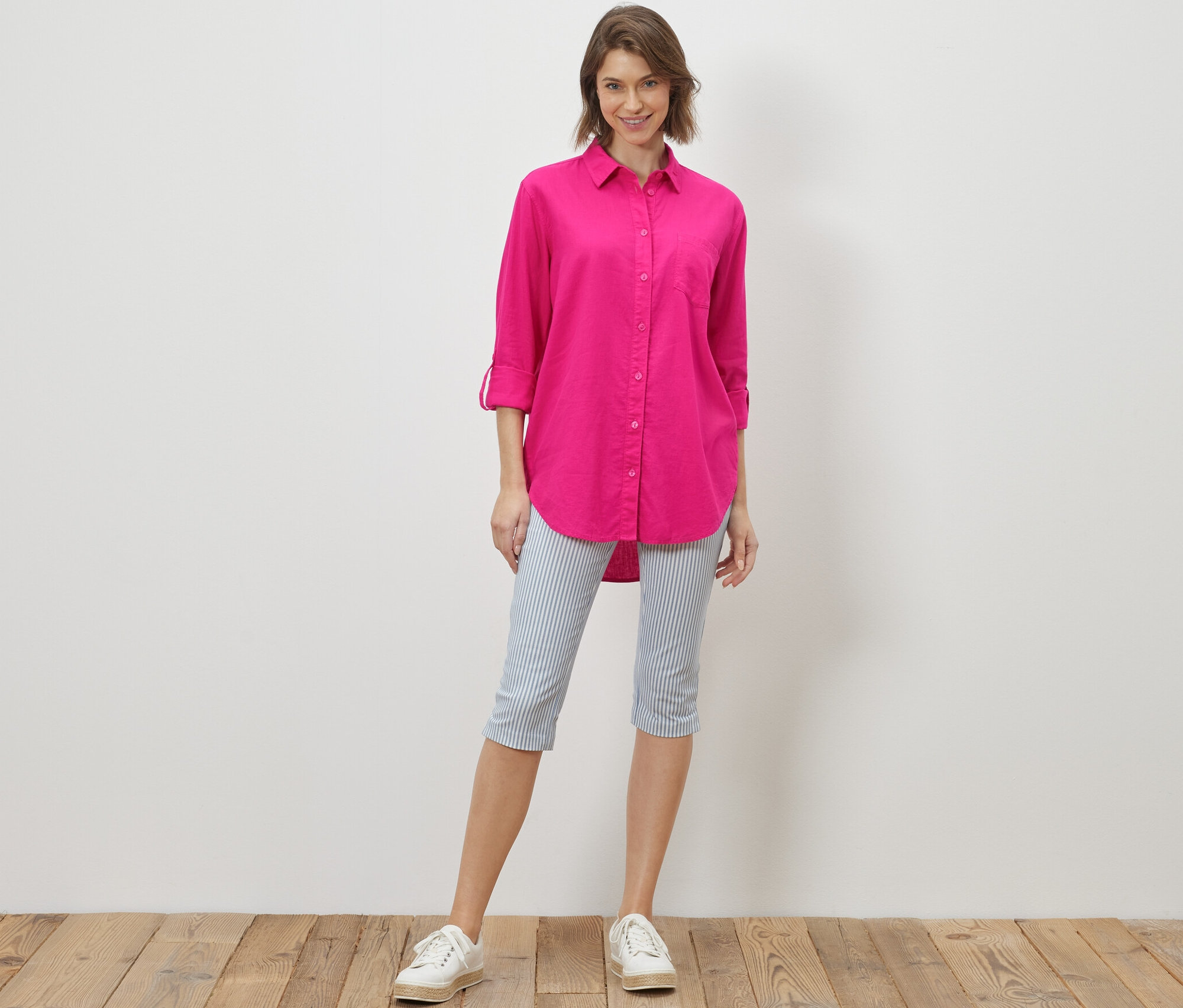 Une femme debout portant une blouse longue en lin rose.