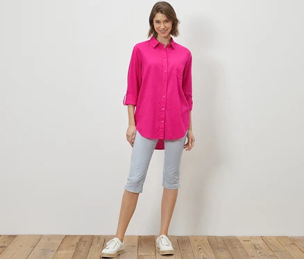Une femme debout portant une blouse longue en lin rose.