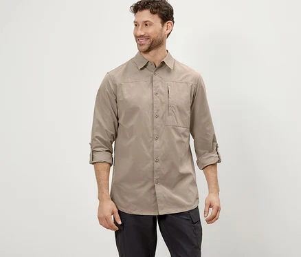 Un homme pose en chemise d’extérieur beige avec protection anti-moustiques et pantalon noir.