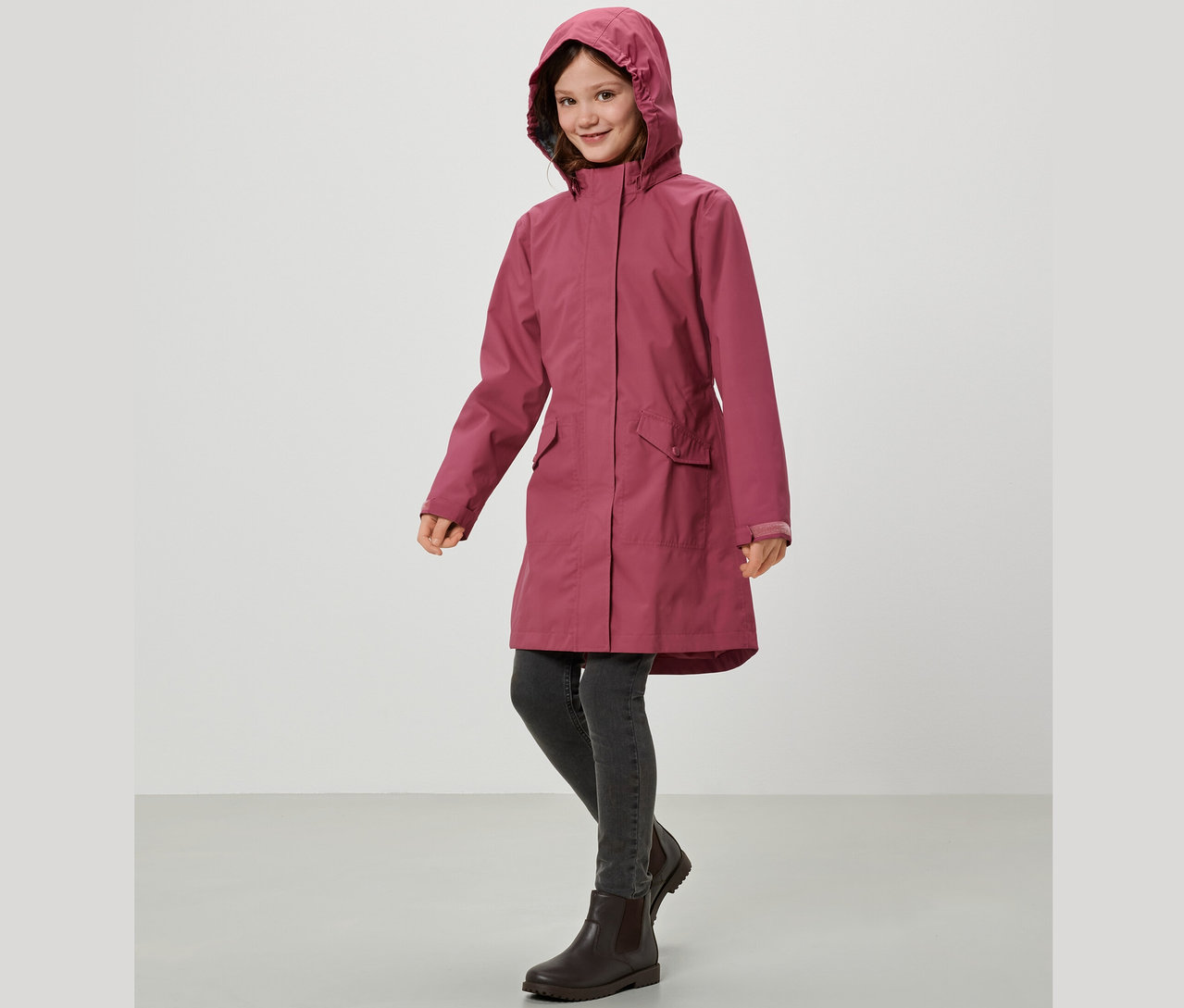 Une fille souriante porte une parka de pluie pour enfants.