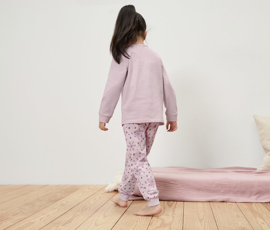 Une fille en pyjama à manches longues avec des flocons de neige marche sur le plancher en bois.