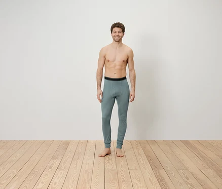 Un homme torse nu se tient sur un plancher en bois et porte un legging gris.