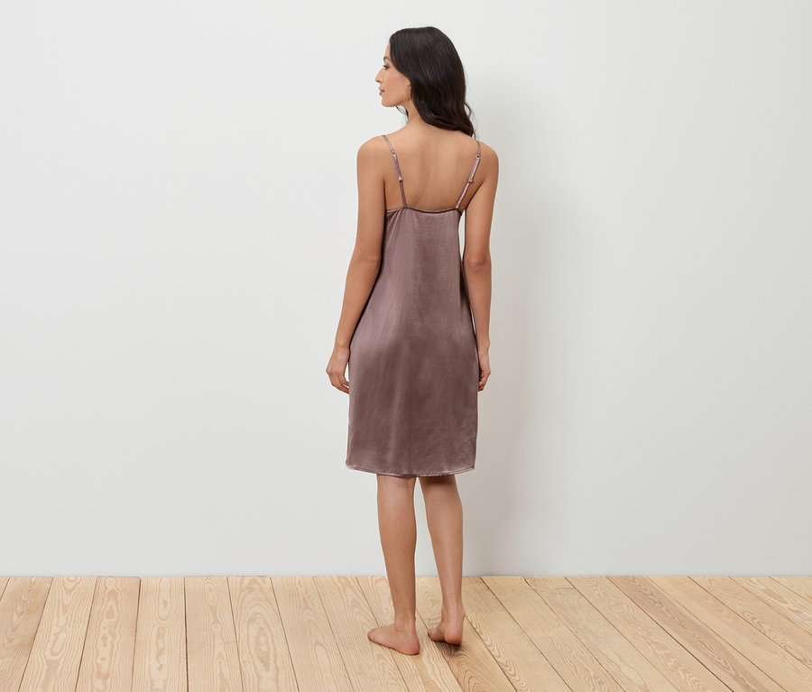 Une femme se tient dos à la caméra et porte une nuisette violette.
