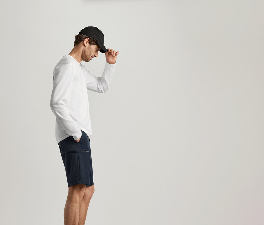 Un homme portant une casquette noire et un short bleu marine porte un 2 Langarmshirts blanc.