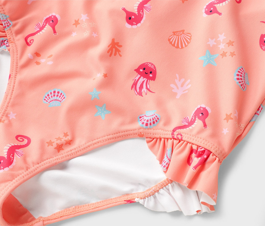 Gros plan sur un maillot de bain saumon avec des motifs d'hippocampes, de méduses et de coquillages.
