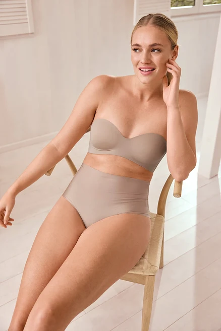 Femme assise sur une chaise de salle à manger en chêne touchant son visage.