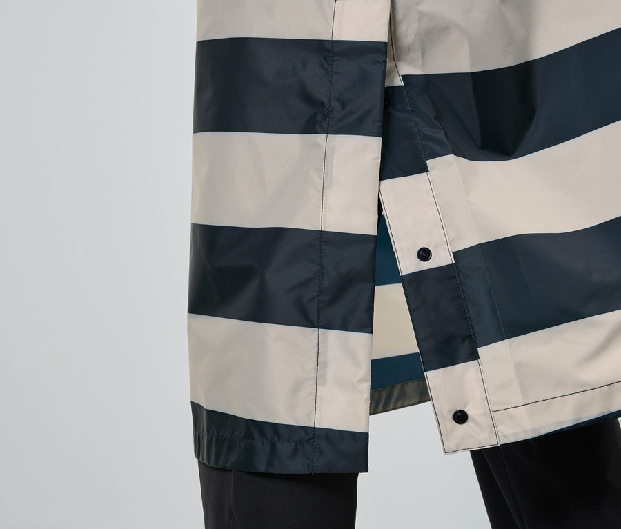 Gros plan sur un imperméable rayé bleu marine et beige, partiellement ouvert, avec des boutons noirs.