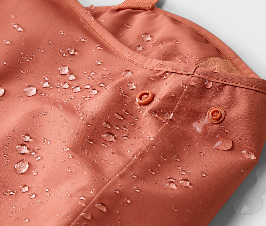 Gros plan sur une veste imperméable couleur terre cuite avec boutons-pression et gouttes d'eau.