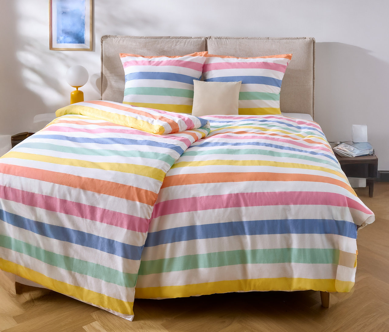 Lit avec des draps rayés multicolores et deux oreillers.
