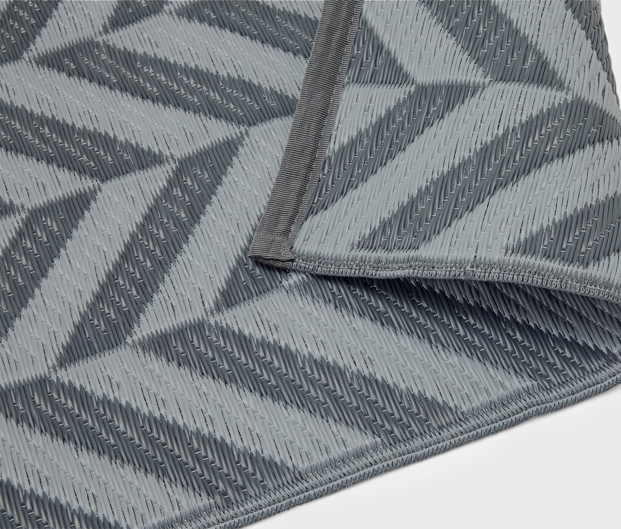 Une couverture de pique-nique grise avec un motif géométrique est pliée sur un fond blanc.