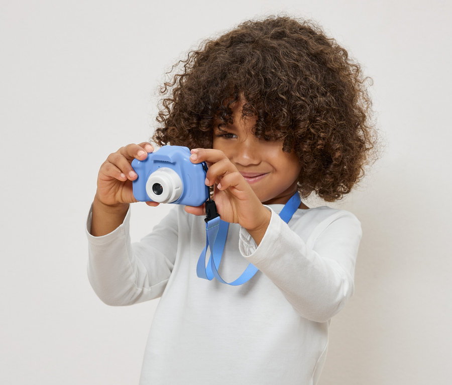 Enfant aux cheveux bouclés tenant un appareil photo jouet bleu.
