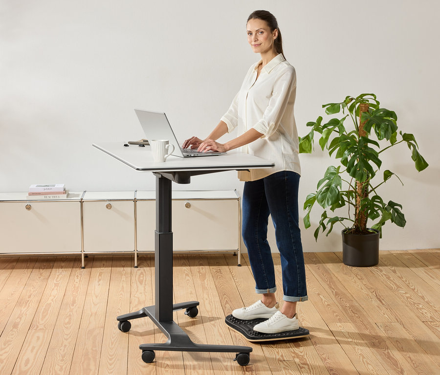 Une femme se tient debout à un bureau à hauteur réglable et utilise un ordinateur portable, une tasse est posée à côté.