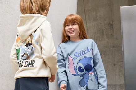 Deux enfants debout devant un mur. Un enfant porte un pantalon de jogging pour enfant et un sweat à capuche avec des personnages de Minecraft. L'autre enfant porte 3 leggings pour enfant, noir, et un t-shirt Stitch.