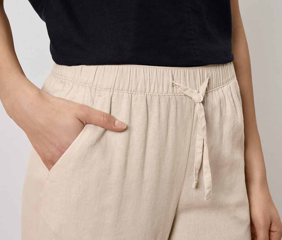 Femme avec la main dans la poche d'un pantalon beige à cordon.