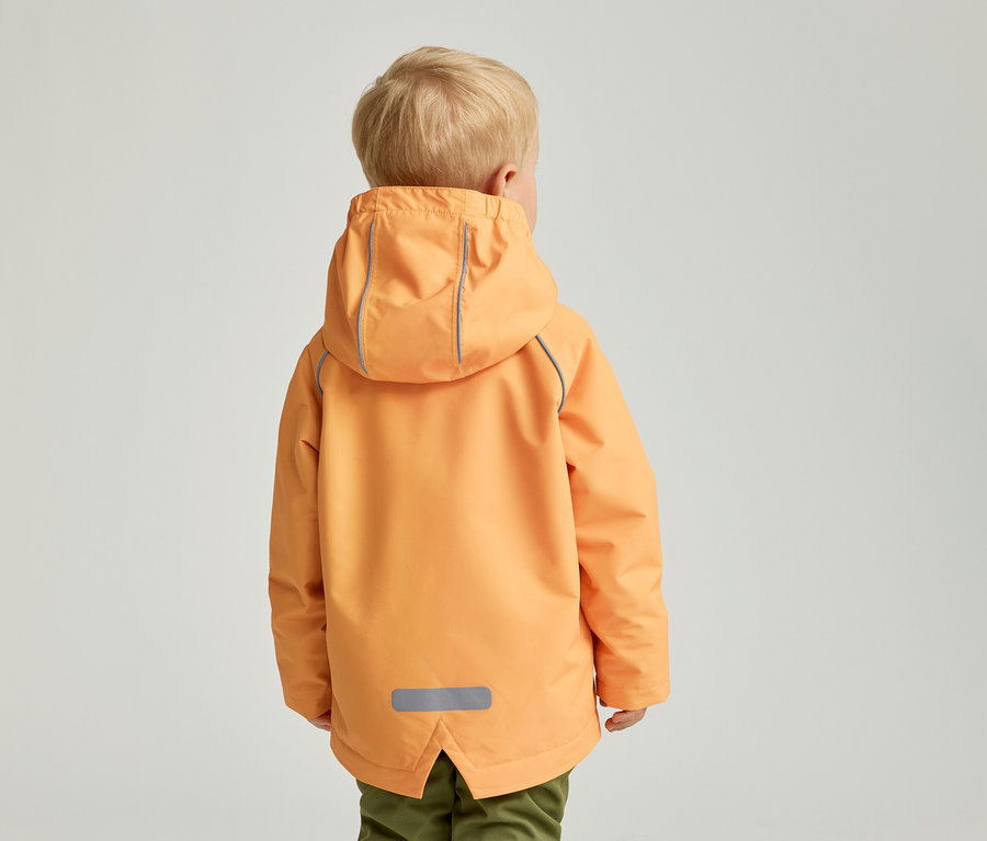 Vue arrière d'un enfant blond portant une veste orange à capuche et un pantalon vert sur un fond clair.