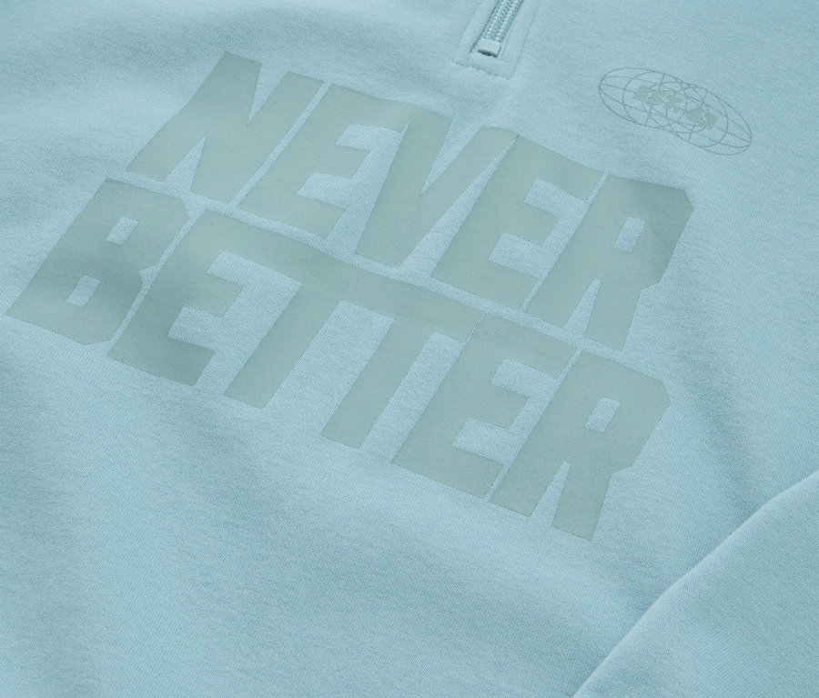 Gros plan d'un sweat-shirt bleu clair avec l'inscription "NEVER BETTER" et une fermeture éclair au niveau du col.