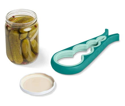 Un bocal de cornichons avec un couvercle ouvert et un ouvre-bocal vert sont posés sur un fond blanc.