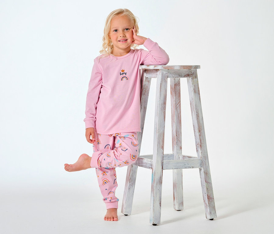Fille portant un pyjama long pour enfant SCHIESSER à motif arc-en-ciel, appuyée sur un tabouret.