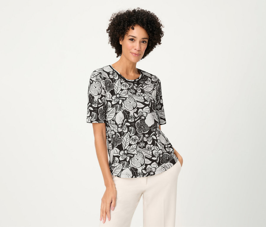 Une femme aux cheveux bouclés porte un T-shirt Olsen à motifs floraux et un pantalon clair.