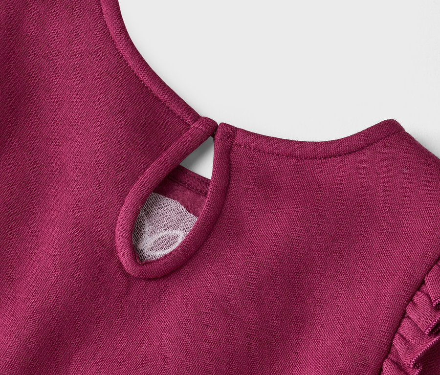 Gros plan d'une robe bordeaux avec des manches à volants et une découpe en forme de goutte d'eau avec un tissu en maille.