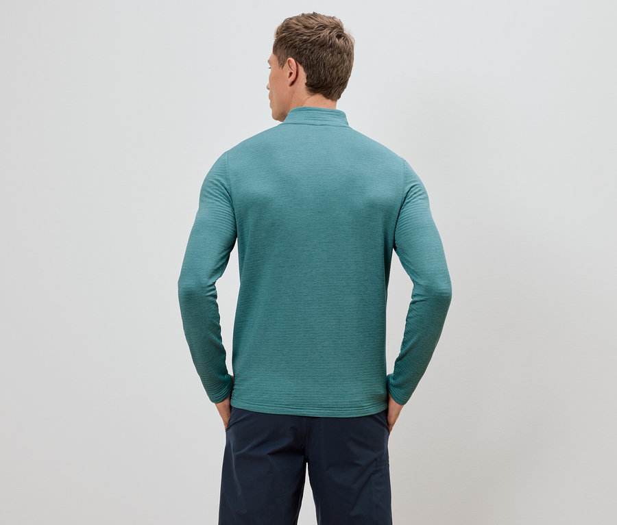 Homme vu de dos portant un haut turquoise à manches longues et un short bleu marine, les mains dans les poches.
