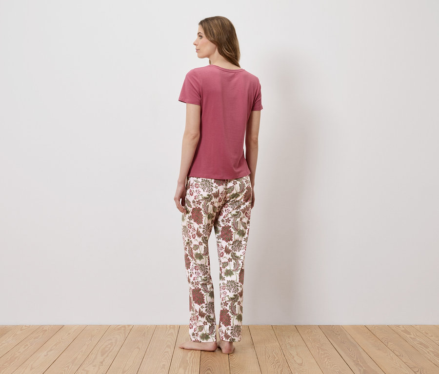 Une femme, vue de dos, porte un t-shirt rose et un pantalon à fleurs.
