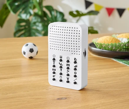 Appareil blanc avec des boutons sur une table en bois, avec un petit ballon de football, des muffins et des décorations de fête en arrière-plan.