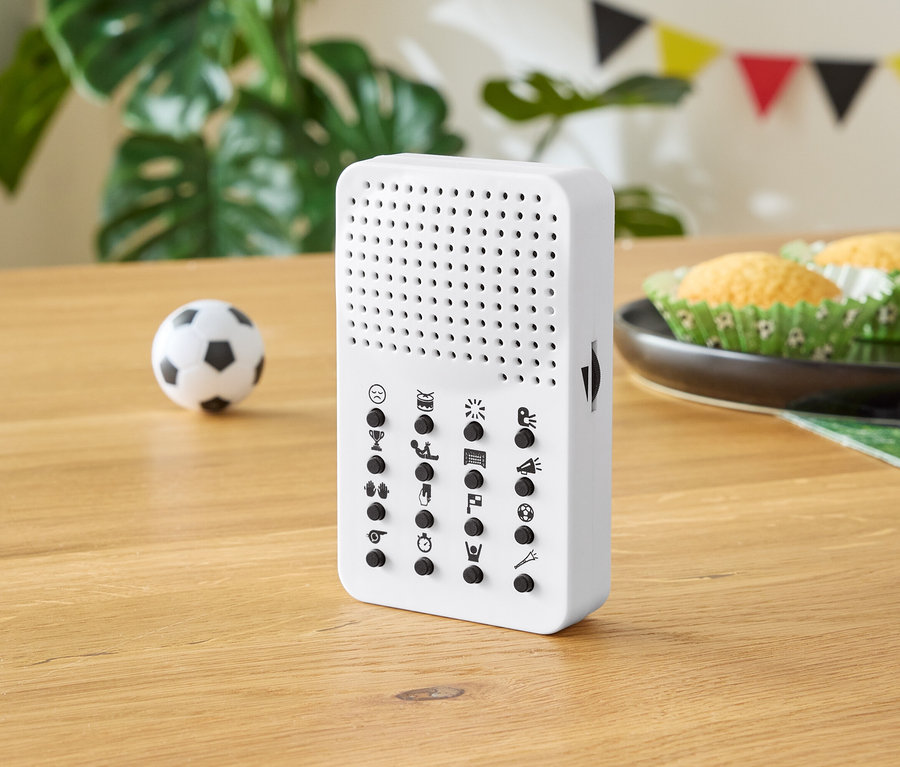 Appareil blanc avec des boutons sur une table en bois, avec un petit ballon de football, des muffins et des décorations de fête en arrière-plan.