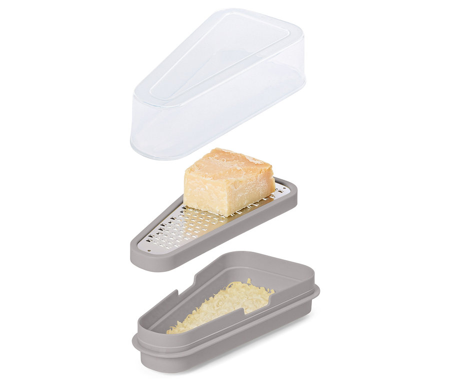 Un set de râpe à fromage gris avec un morceau de fromage sur la râpe, du fromage râpé dans le récipient et un couvercle transparent au-dessus.