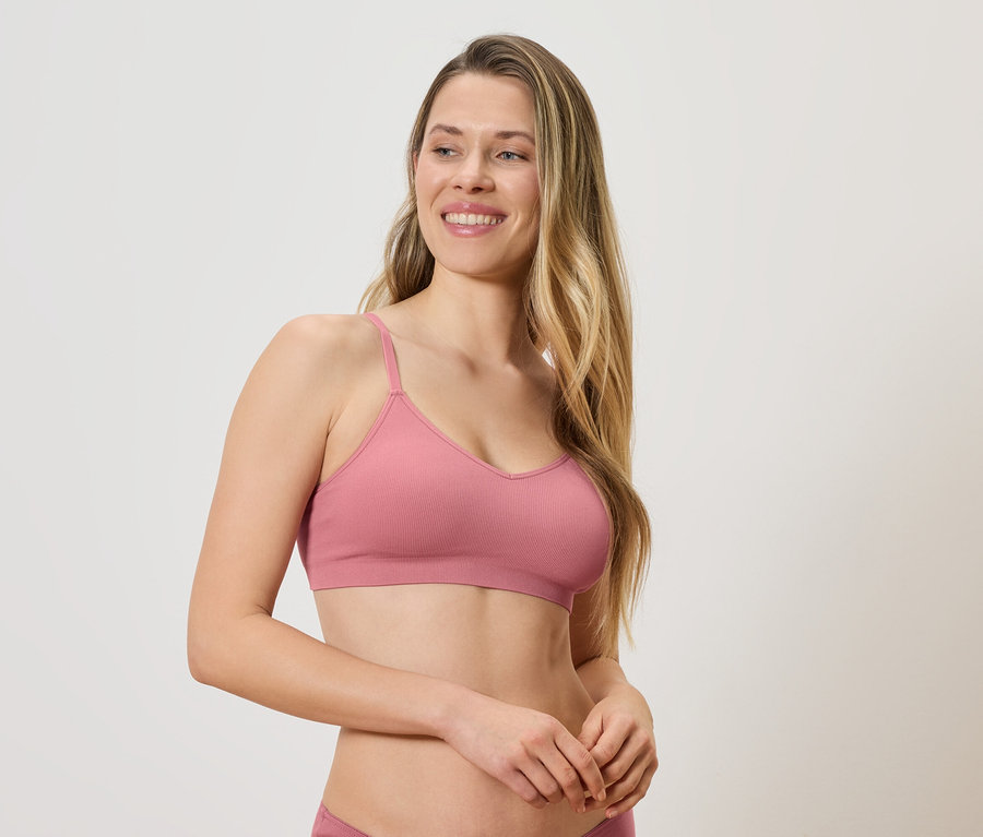 Une femme aux longs cheveux blonds, portant un soutien-gorge et une culotte roses, regarde sur le côté.
