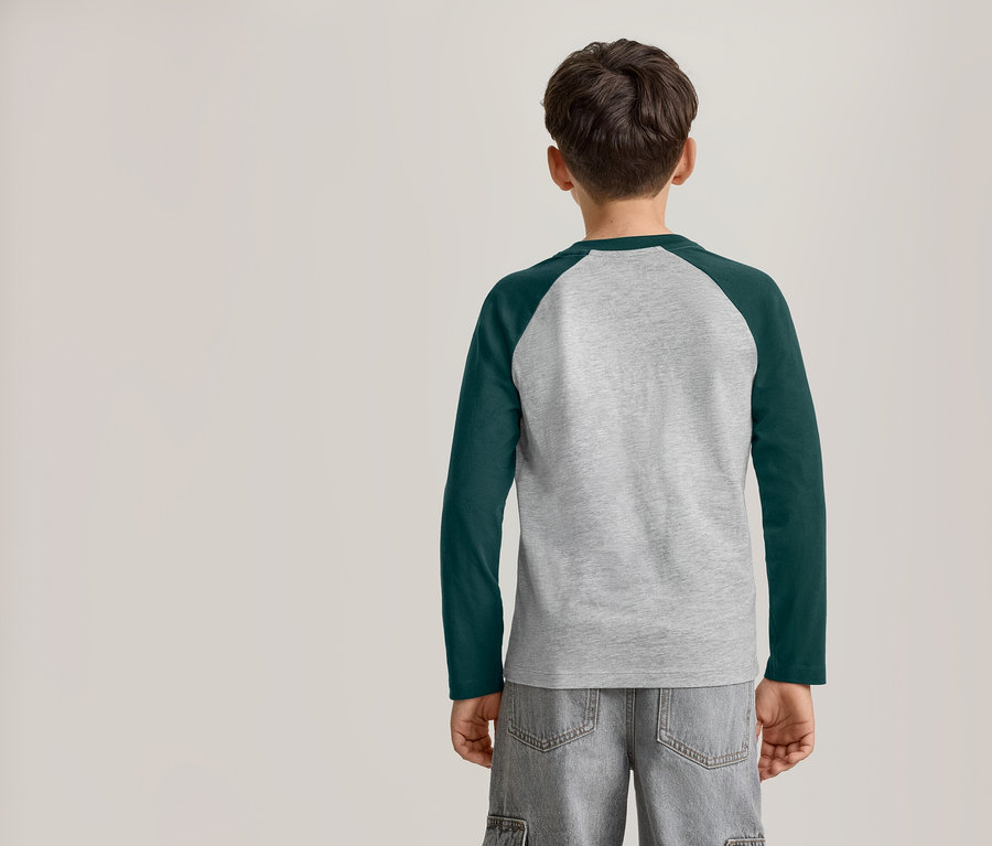 Un jeune garçon vu de dos, portant un t-shirt raglan à manches longues gris et vert foncé et un short gris.