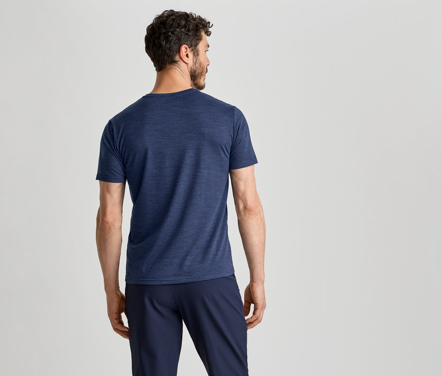 Un homme vu de dos, portant un t-shirt bleu foncé et un pantalon bleu foncé, regardant vers la droite.