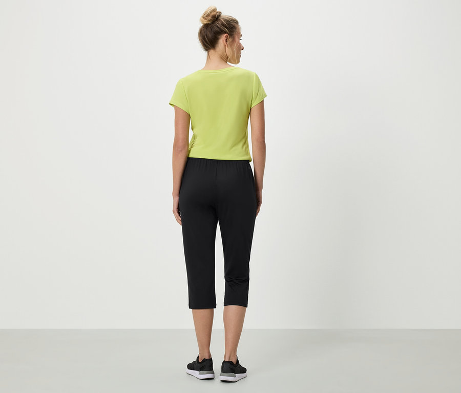 Femme vue de dos portant un t-shirt vert clair, un pantacourt noir et des baskets.